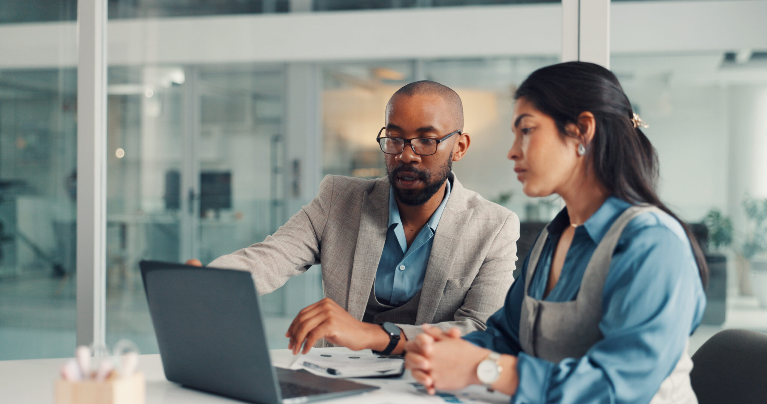 Two people working on a laptop together, viewing the screen and gesturing toward it.